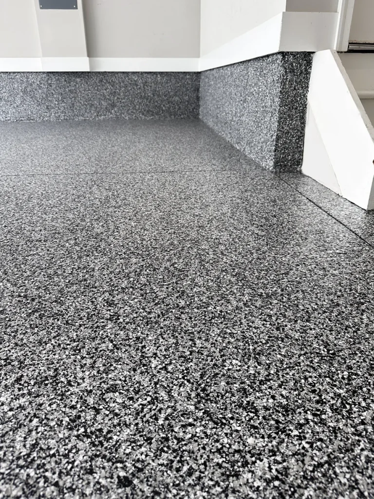 Close-up of a gray flake epoxy garage floor and coated stem wall at the garage steps